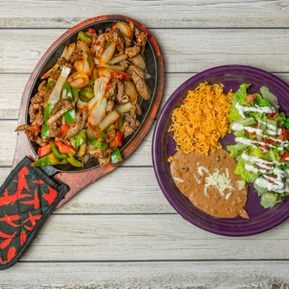 Sizzling beef fajitas with onions and peppers, alongside rice, refried beans, and a side salad.