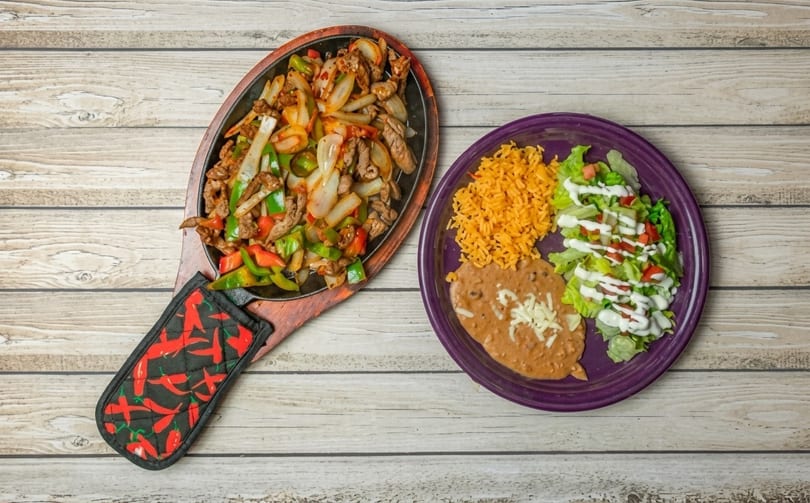 Sizzling fajitas with beef, peppers, and onions, alongside rice, refried beans, and salad.